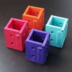 four different colored plastic containers sitting on a black surface with holes in the bottom and sides