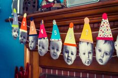 a bunch of birthday hats hanging from a line on a fireplace mantel with pictures of babies in them