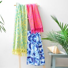 three towels hanging on a clothes rack next to a potted plant and wooden stool