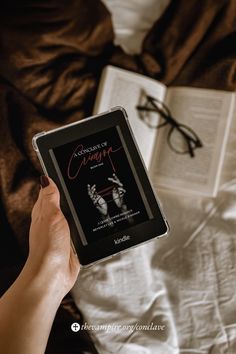 a person holding an electronic device in their hand while reading a book on top of a bed