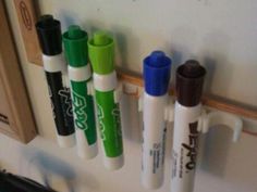 several pens are lined up on the wall next to each other, with one green marker in between them