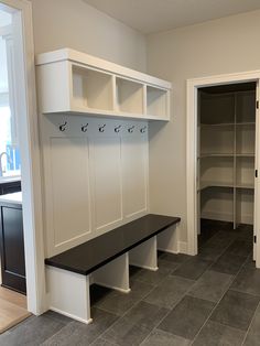 an empty room with white cabinets and black bench in the center, and gray tile on the floor