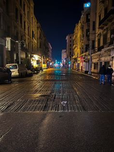 an empty city street at night with people standing on the sidewalk