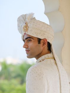 a man wearing a white turban and standing next to a wall with trees in the background