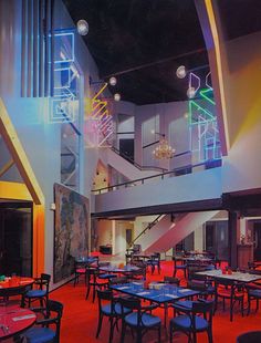 an indoor dining area with tables, chairs and chandeliers on the ceiling is lit by multicolored lights