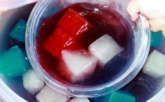 someone is holding a plastic container filled with ice cubes and red liquid in it