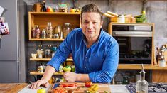 a man standing in front of a cutting board with vegetables on it and an oven behind him