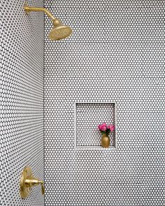 a white tiled shower with gold fixtures and pink flowers