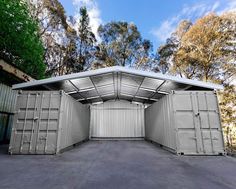 an open metal storage shed in the middle of a parking lot with lots of trees