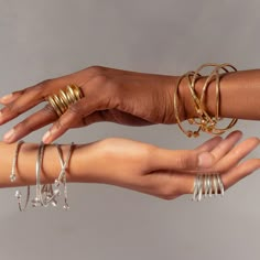 two hands holding different types of rings and bracelets on each arm, with one hand in the other