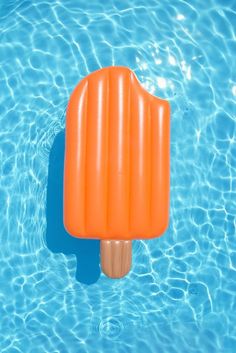 an orange popsicle floating on top of a pool