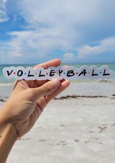 a person holding up a piece of paper with the word volleyball written on it in front of an ocean