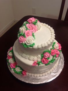 three tiered white cake with pink and green flowers on the top, sitting on a table