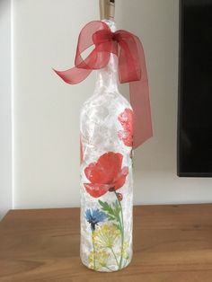 a glass bottle with flowers painted on it and a red ribbon tied around the top