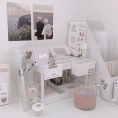 a white desk topped with lots of drawers and pictures next to a cup filled with liquid