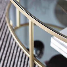 a glass and gold coffee table with books on the bottom, next to a rug