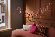 a pink couch sitting next to a window in a living room with christmas decorations hanging on the wall