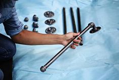 a person is holding a metal rod and some screws on a blue sheeted surface