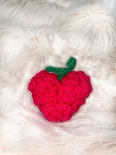 a red crocheted apple laying on top of a white fur covered bedding