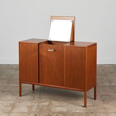 a small wooden cabinet with a mirror on it's top and bottom section, in front of a white wall