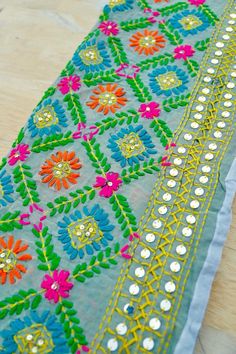 an embroidered cloth with colorful flowers on it sitting on top of a wooden table next to a pair of scissors