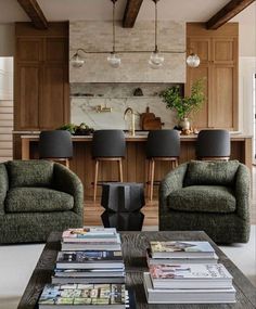 a living room filled with furniture and a kitchen in the back ground behind two green chairs