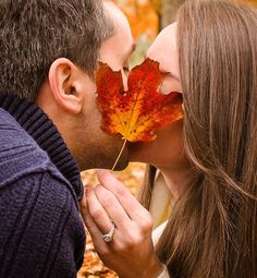 a man and woman kissing with autumn leaves