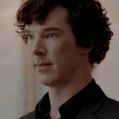 a close up of a person wearing a suit and tie with curly hair looking at the camera