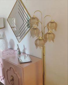 a pink and gold dresser with a mirror on the wall next to an ornate lamp