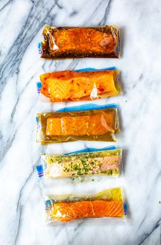 four bags of fish fillets lined up on a marble counter top with seasoning