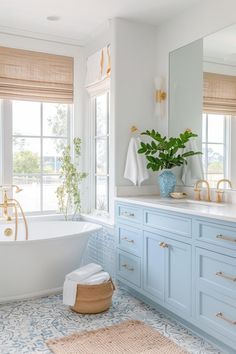 a bathroom with blue cabinets and a white bathtub next to a window filled with plants