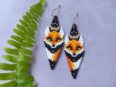 the beaded earrings are decorated with orange and black fox heads on them, along with a fern leaf