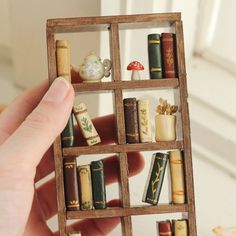 a hand holding a miniature book shelf filled with books and knick - knacks