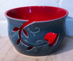 a red and gray bowl sitting on top of a wooden table next to a white wall