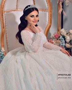 a woman in a white dress sitting on a chair wearing a tiara and posing for the camera