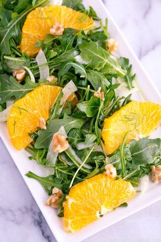 a white plate topped with orange slices and green leafy salad on top of a marble counter