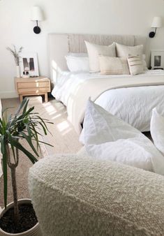 a bed with white sheets and pillows next to a potted plant on the floor