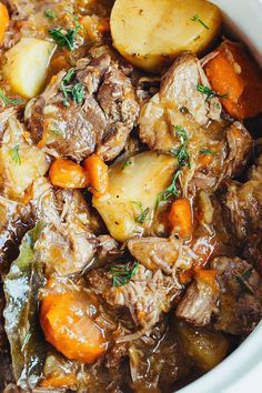 beef stew with carrots, potatoes and parsley in a white crock pot