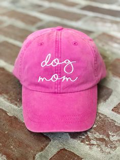 a pink hat with the word dog mom written in white on it sitting on a brick floor