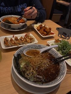 a table topped with plates of food and bowls filled with meat, noodles and veggies