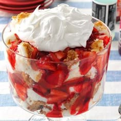 a trifle with strawberries and whipped cream in a glass dish on a table