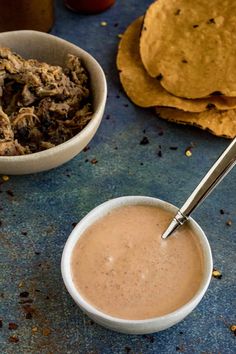 two bowls filled with food next to tortilla chips and salsa dressings on a blue surface