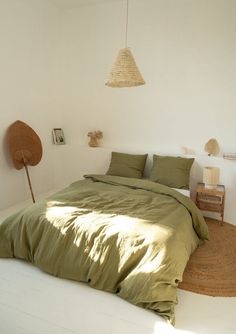 a bed with green sheets and pillows in a room next to a wall mounted fan