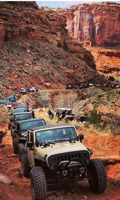 four jeeps driving down a dirt road in the desert with mountains and cliffs behind them