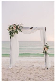 an outdoor wedding setup on the beach with white draping and pink flowers at the top