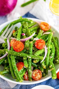 a white bowl filled with green beans, tomatoes and other veggies on top of a blue table cloth