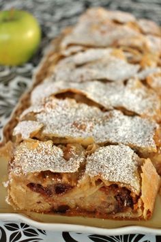 a pastry on a plate with an apple in the backgroung and powdered sugar on top