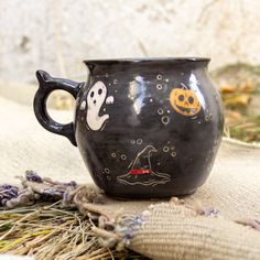 a black mug with ghost faces on it sitting next to some dried grass and other items