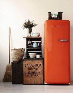 an orange refrigerator sitting in front of a wooden crate with dishes on top of it