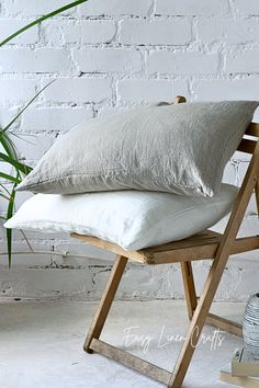 a wooden chair with two white pillows on it and a potted plant next to it